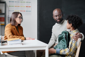 A teacher meets with a student and their parent in the classroom.